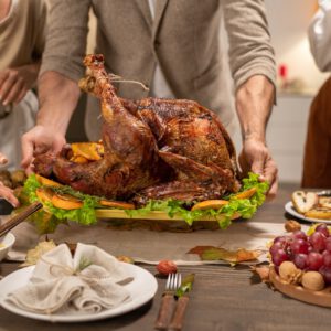 Hands of mature man putting tray with big roasted homemade turkey on table