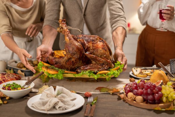 Hands of mature man putting tray with big roasted homemade turkey on table