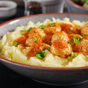 Meatballs in tomato sauce with mashed potatoes in bowl.